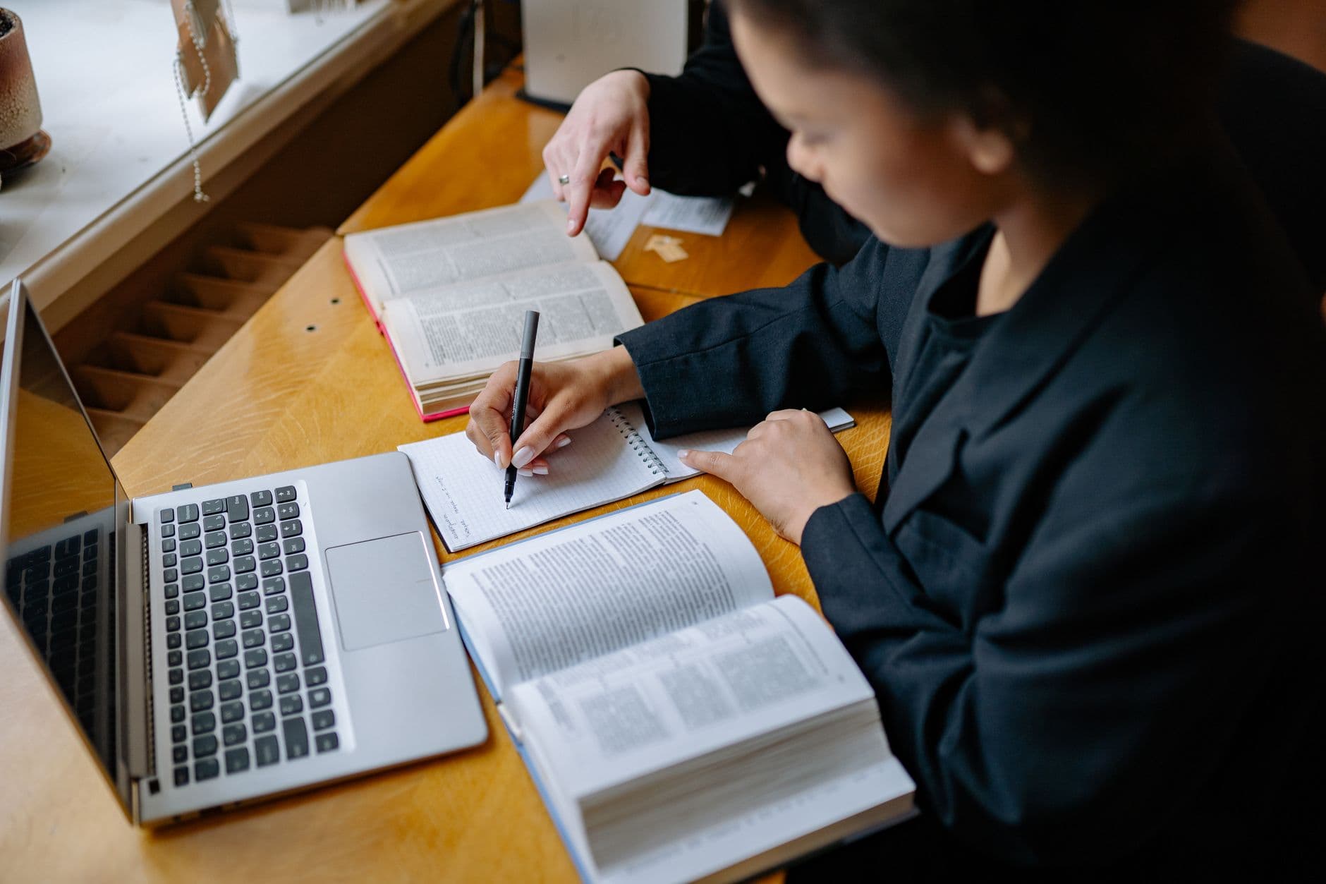 A student taking notes beside a laptop and an open textbook